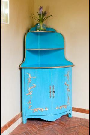 Rinconera realizada artesanalmente, en madera de cerezo. Con 3 baldas y doble puerta en la parte inferior con cerradura de forja. Pintada a mano.